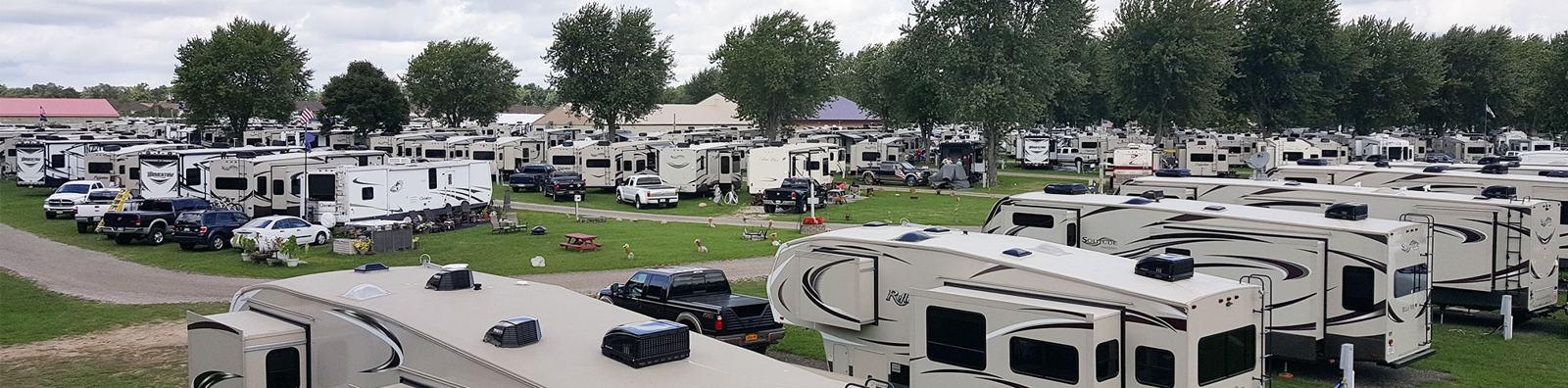 Panorama of the RV sites: rows of fifth-wheel trailers and trucks under tall shade trees