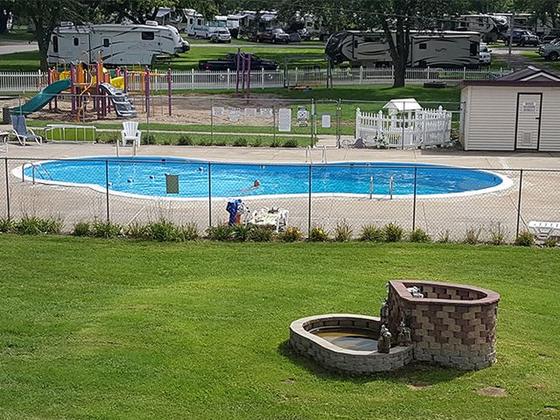 Lawn with a stone fire ring in front of the fenced pool and playground