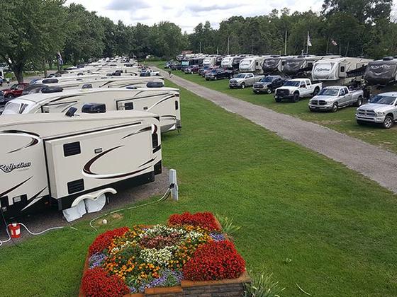 Travel trailers parked along a gravel lane, with a bed of red and orange flowers in front