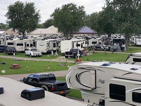 Long rows of fifth-wheel trailers and pickup trucks parked on grass sites under mature trees